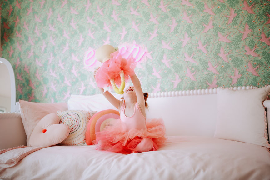 little girl playing on bed with dolls with pink and green wallpaper from Anthropologie