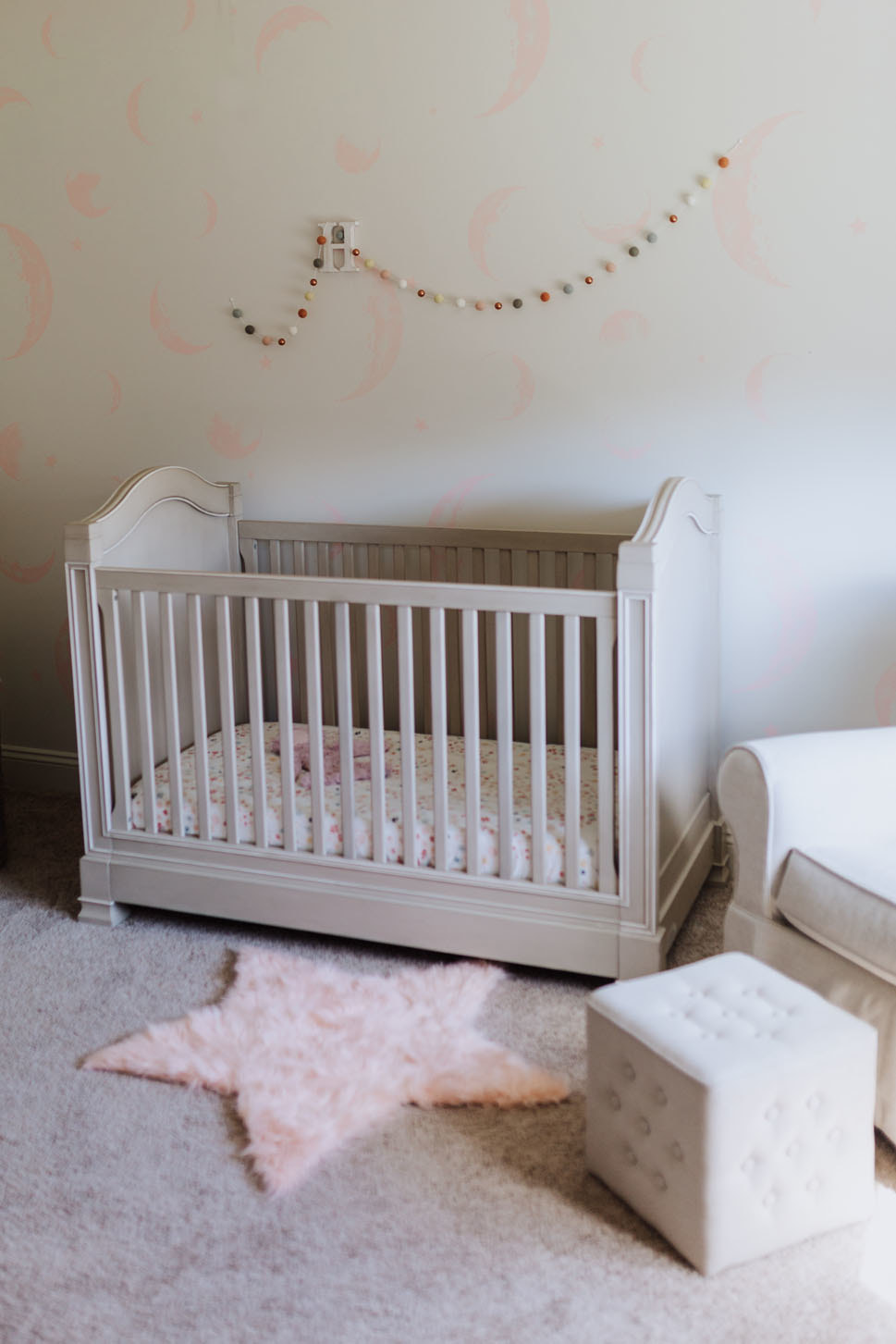 Custom painted moon mural behind crib in a pretty pink and white baby girl nursery
