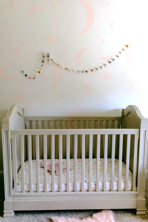 Custom painted moon wall mural behind crib of pretty pink and white baby girl nursery